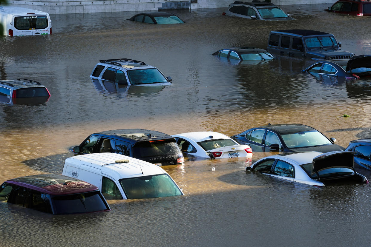 A dozen and a half vehicles appear parked near one another, all partially submerged in brown water.