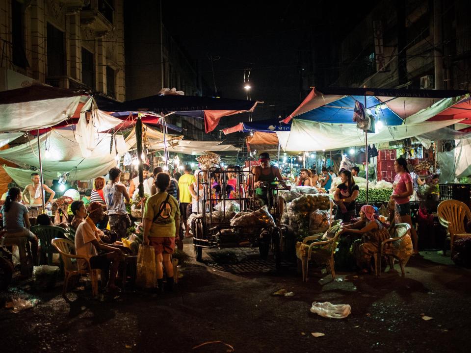 A busy area of Divisoria market where people are sitting in plastic chairs and inspecting stalls of goods.