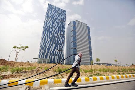 A labourer pulls a cable in front of two office buildings in Gujarat International Finance Tec-City (GIFT) at Gandhinagar, in the western Indian state of Gujarat, April 10, 2015. REUTERS/Amit Dave