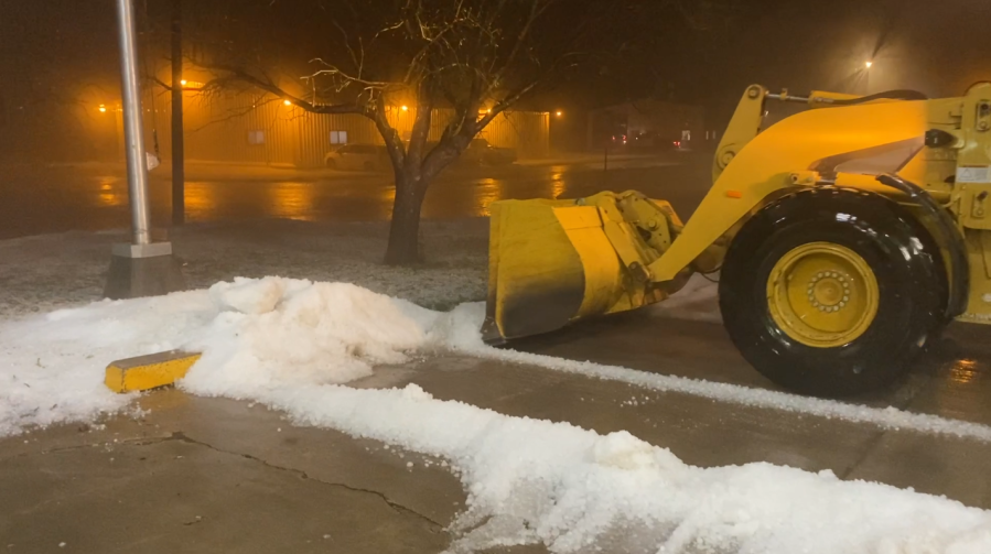 A front-end loader scoops up mounds of hail