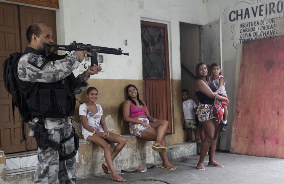 Residents observe a police officer take up position during an operation at the Mare slums complex in Rio de Janeiro