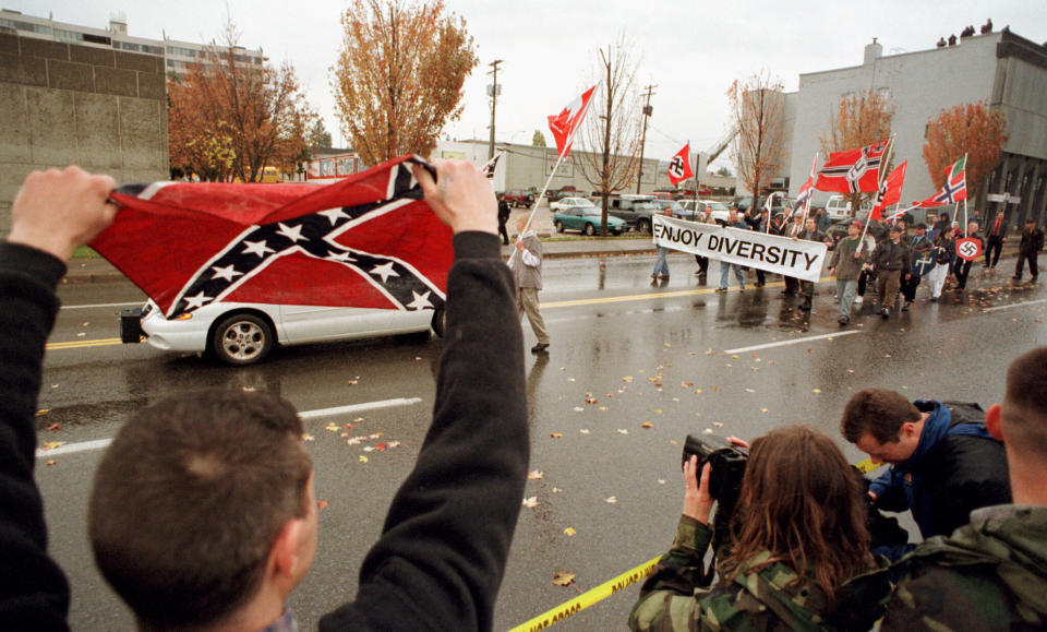 An unidentified supporter waves a Confederate flag while members of the Aryan Nations carry Nazi flags and a banner saying "Enjoy Diversity" during a parade in downtown Coeur d'Alene, Idaho, on Oct. 28, 2000. (Photo: REUTERS/Jeff T. APB/RCS)