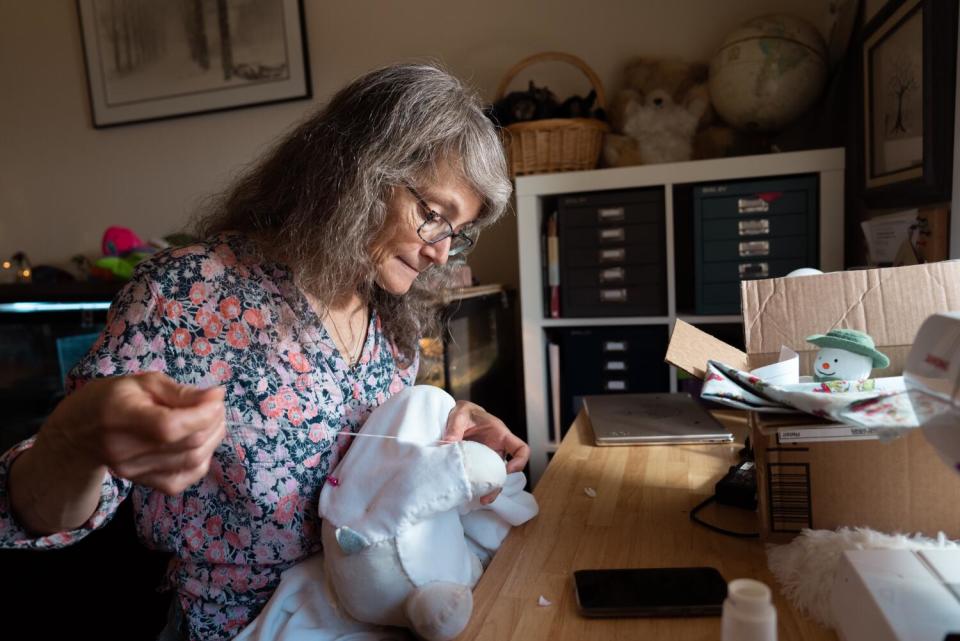 A woman sews a toy snowman at her home.