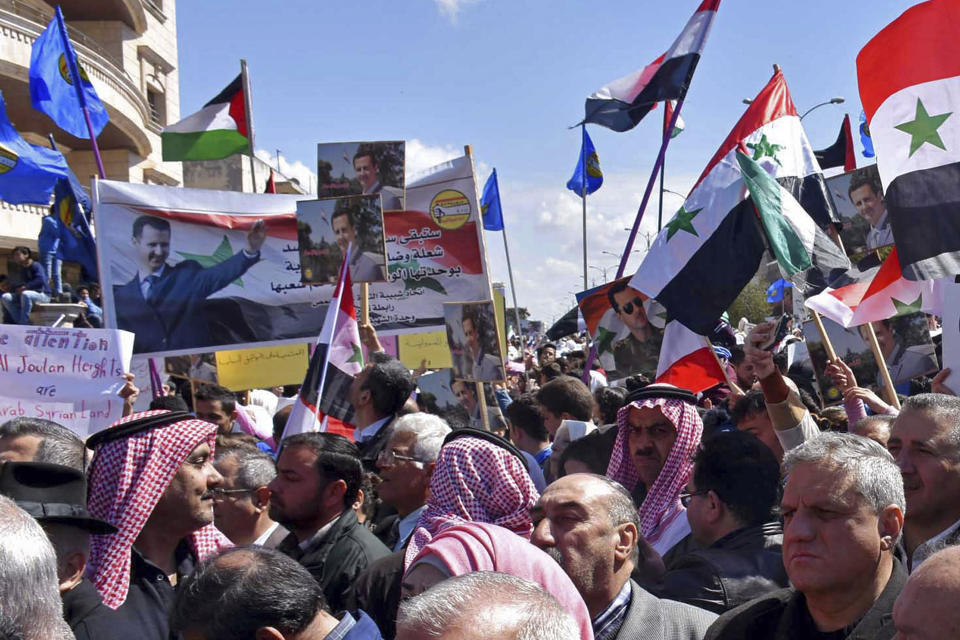 In this photo released by the Syrian official news agency SANA, Syrians hold national flags and portraits of Syrian President President Bashar Assad during a protest against President Donald Trump's move to recognize Israeli sovereignty over the occupied Golan Heights, in Homs, Syria, Tuesday, March 26, 2019. Syria's state news agency says thousands of Syrians have held gatherings in the streets of different cities to protest Trump's signing of a declaration reversing US policy on the Golan Heights. (SANA via AP)