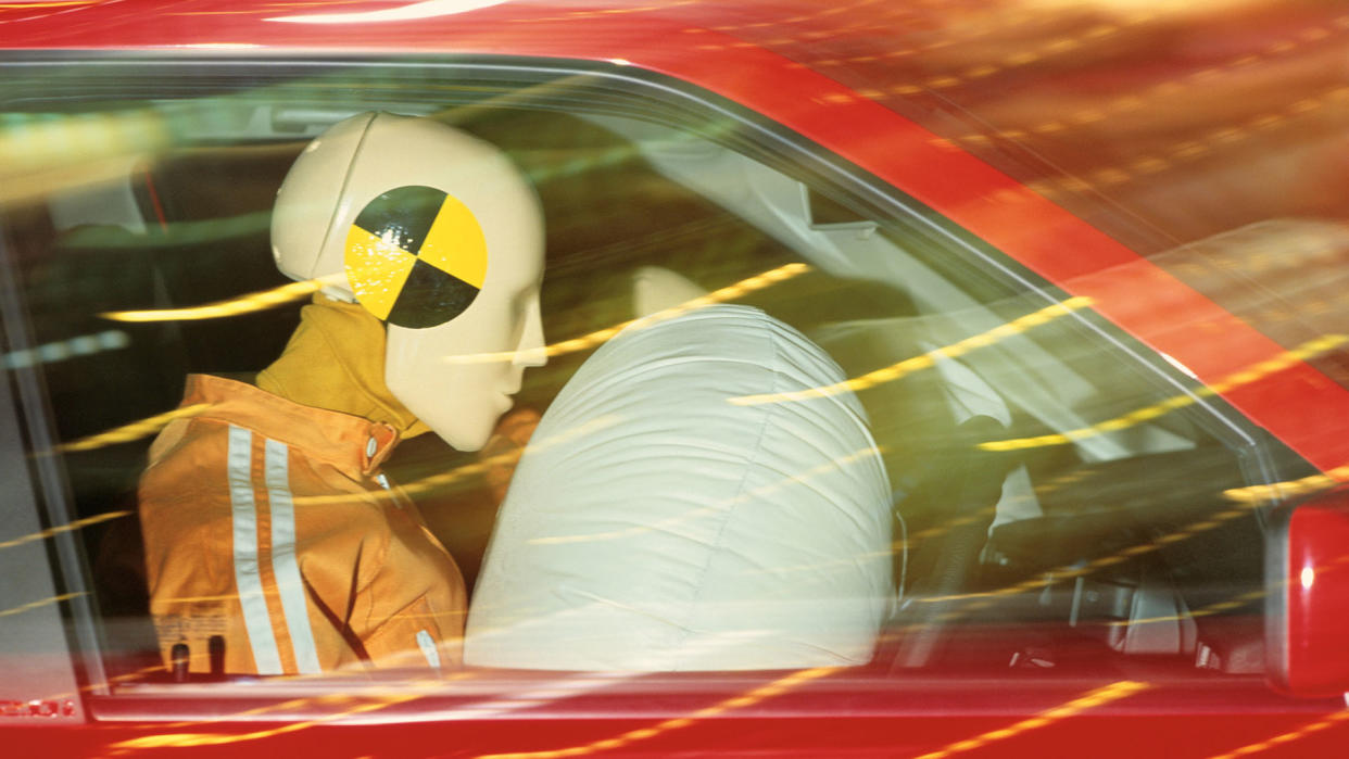  Image shows a crash test dummy in a red car with an airbag inflated 