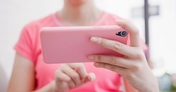 A woman in a pink shirt plays a game on a smartphone with a matching pink cover.