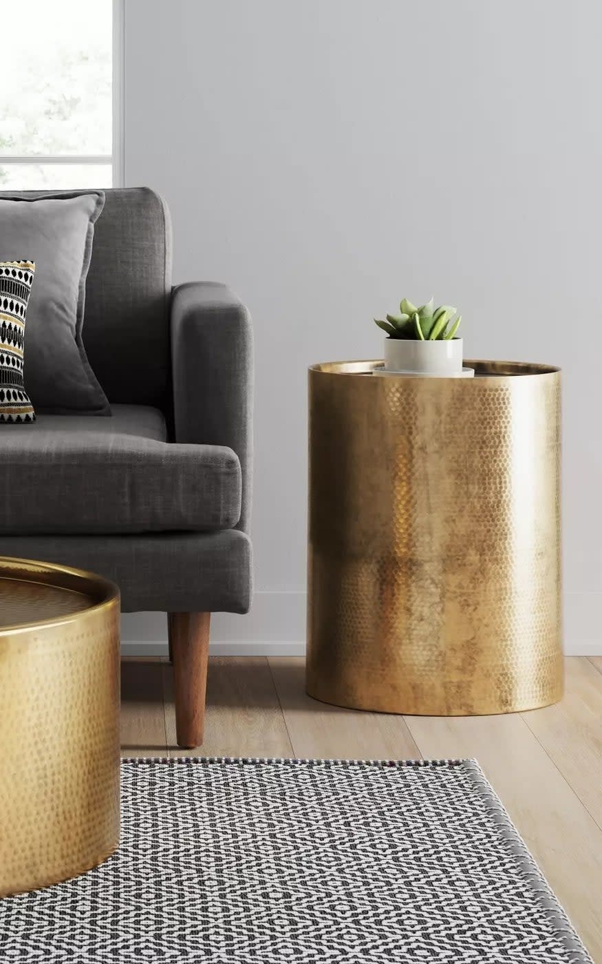 A cylindric gold accent table in a living room with a hammered exterior