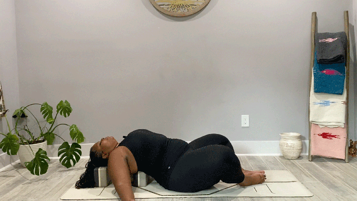 Woman lying on her back on a yoga mat with blocks beneath her upper back in Reclining Bound Angle