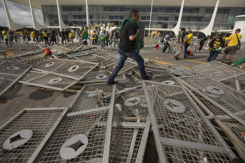 A supporter of former President Jair Bolsonaro steps over downed barricades.