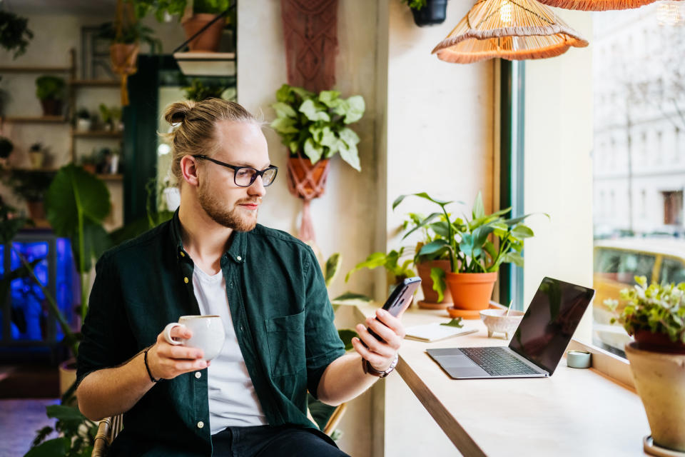 A student using his smartphone while taking a break from work with a coffee in a local café.