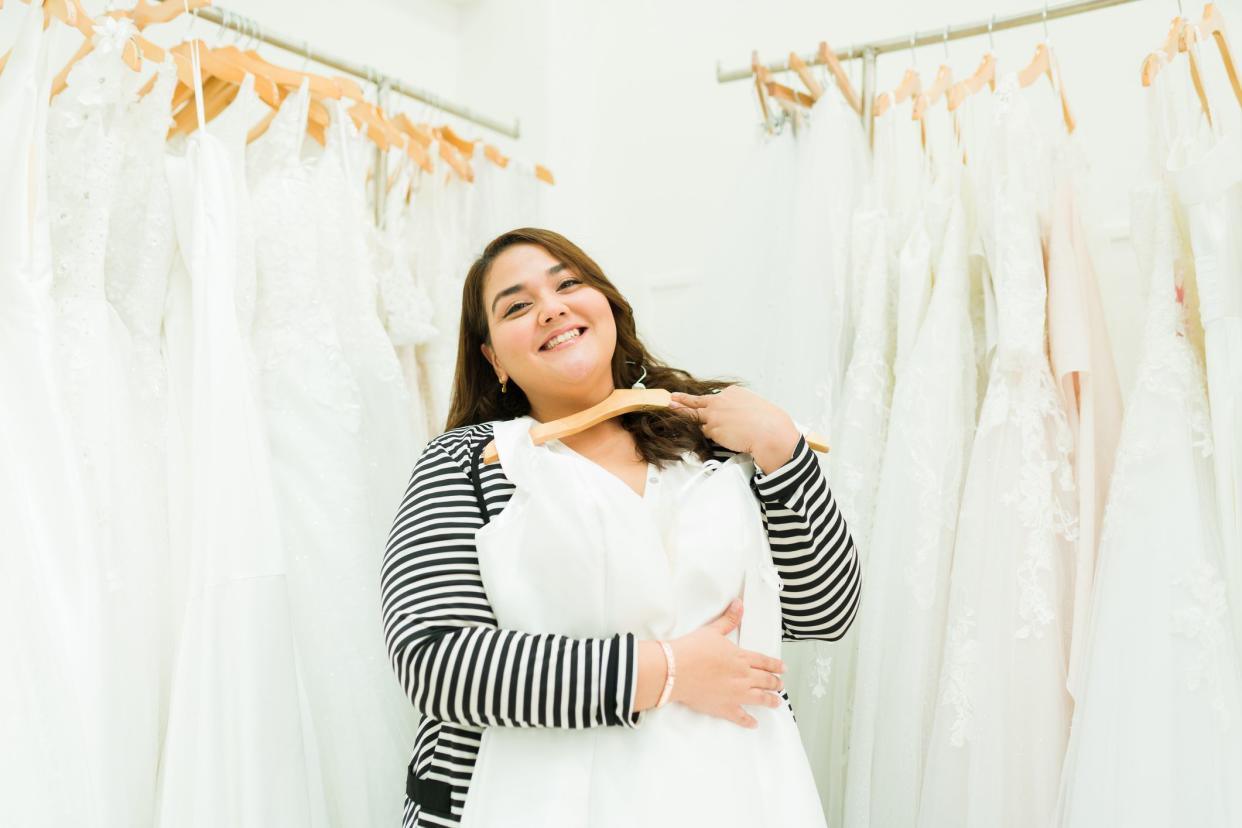 Beautiful chubby woman choosing a beautiful wedding dress and making eye contact while shopping at the bridal store