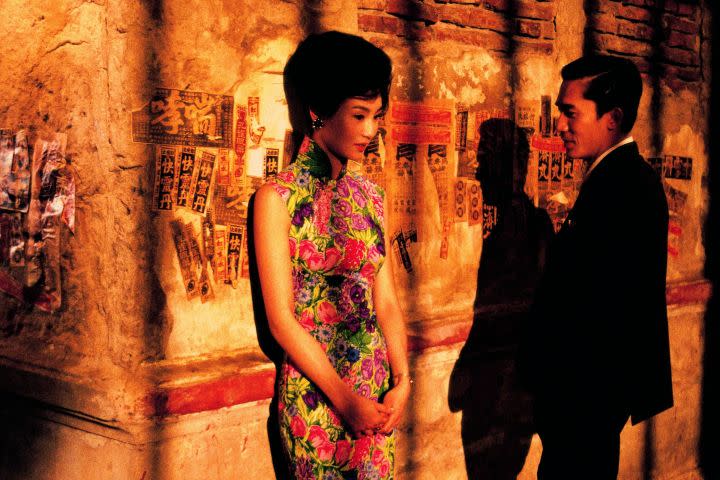 Maggie Cheung leaning against a wall and Tony Leung Chiu-wai looking at her from a scene in In the Mood for Love (2000)