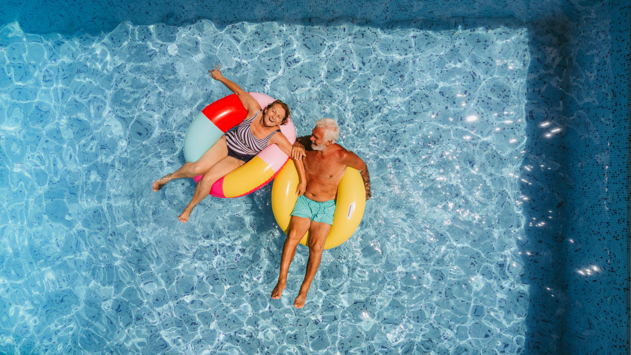 Photo of a senior couple floating on inflatable rings in the swimming pool and enjoying their golden years
