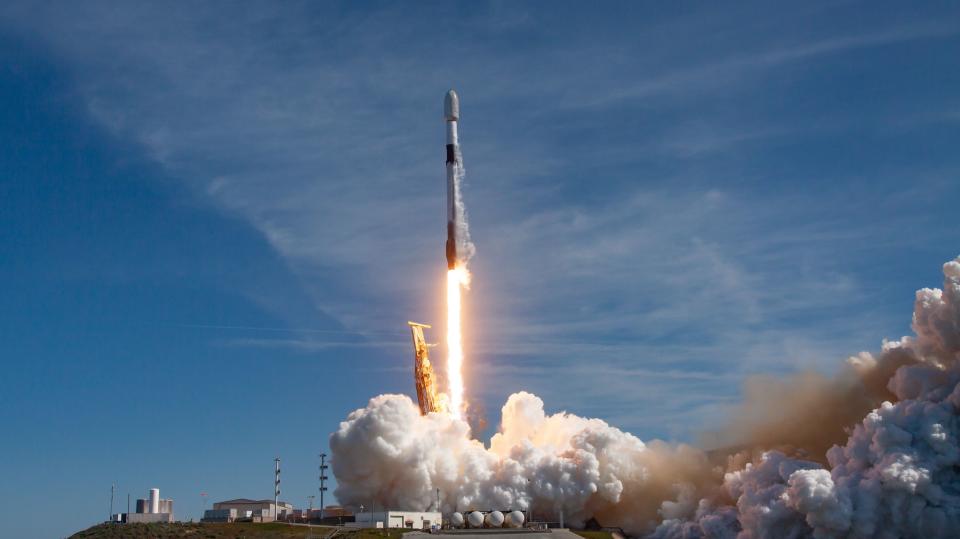 a black-and-white spacex falcon 9 rocket launches into a blue sky