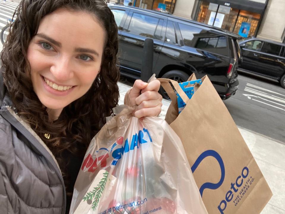 A woman holds up two shopping bags, one from Petco and one from PetSmart.