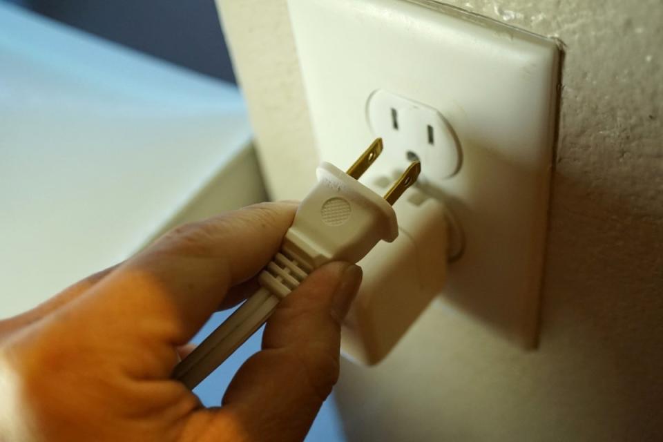 Person unplugging electrical cord from socket