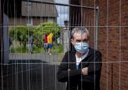 CAPTION CORRECTS THE NAME - Iulian, Romanian worker who stands behind the fence that was set up at the entrance of a housing of Romania slaughterhouse workers in Rosendahl, Germany, Tuesday, May 12, 2020. Hundreds of the workers were tested positive on the coronavirus and were put on quarantine. (AP Photo/Michael Probst)