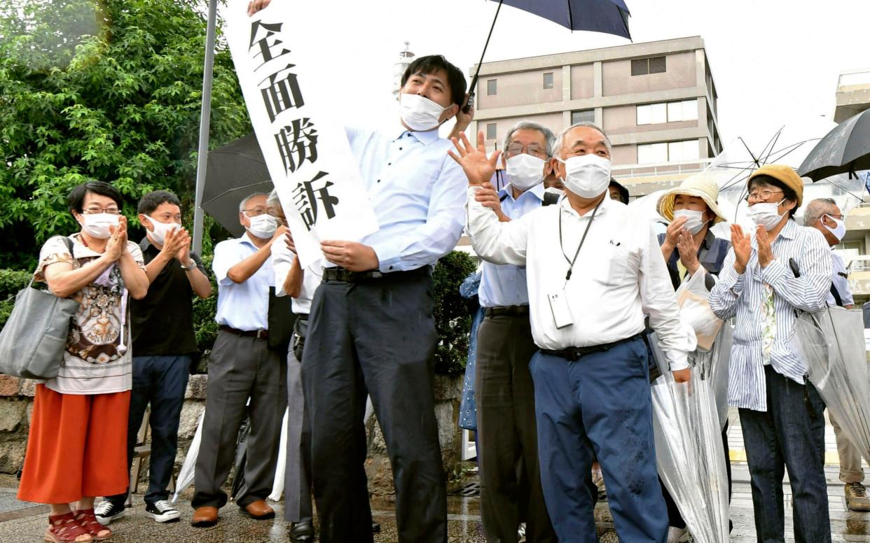 The plaintiffs celebrate outside a court in Hiroshima, holding up a banner which reads 'Overall Victory' - 115323+0900/ Kyodo News