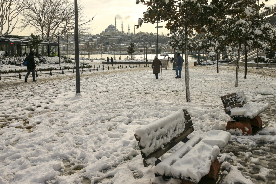 People walk over the Golden Horn with Suleymaniye Mosque in the background at Istanbul, Tuesday, Jan. 25, 2022. Rescue crews in Istanbul and Athens on Tuesday cleared roads that had come to a standstill after a massive cold front and snowstorms hit much of Turkey and Greece, leaving countless people and vehicles in both cities stranded overnight in freezing conditions.(AP Photo/Emrah Gurel)