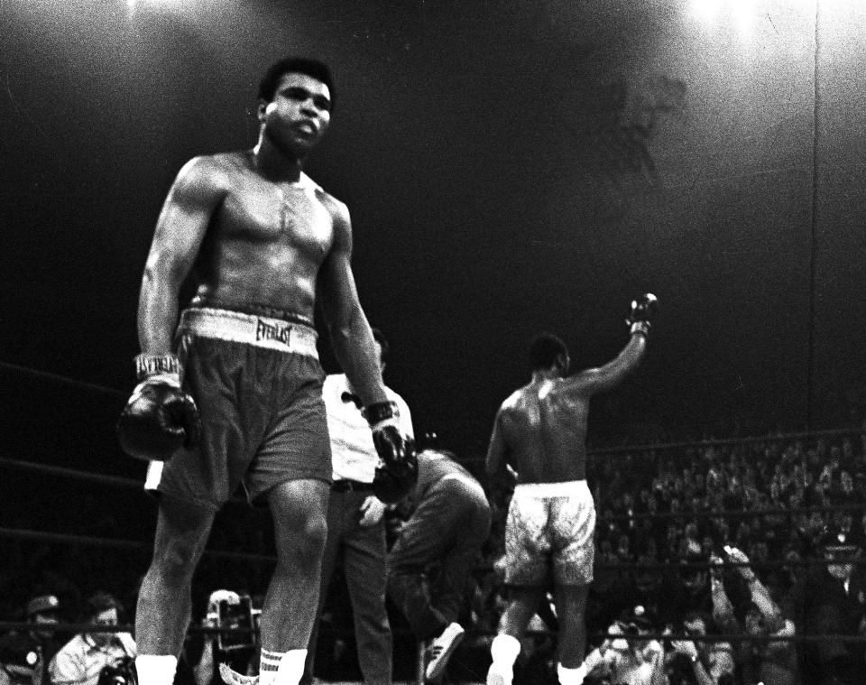 <p>A battered Muhammad Ali walks back to his corner as a triumphant Joe Frazier, background, celebrates his title defense after the 15th round of their title bout at New York’s Madison Square Garden on March 8, 1971. (AP Photo)</p> 