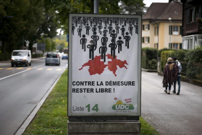 People walk past an electoral poster of the far-right party UDC SVP reading in French "Against excess, remain free" in Yverdon, Western Switzerland on September 23, 2015 (AFP Photo/Fabrice Coffrini)