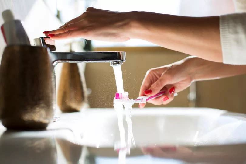 Woman rinsing her toothbrush, close-up of hands - stock photo