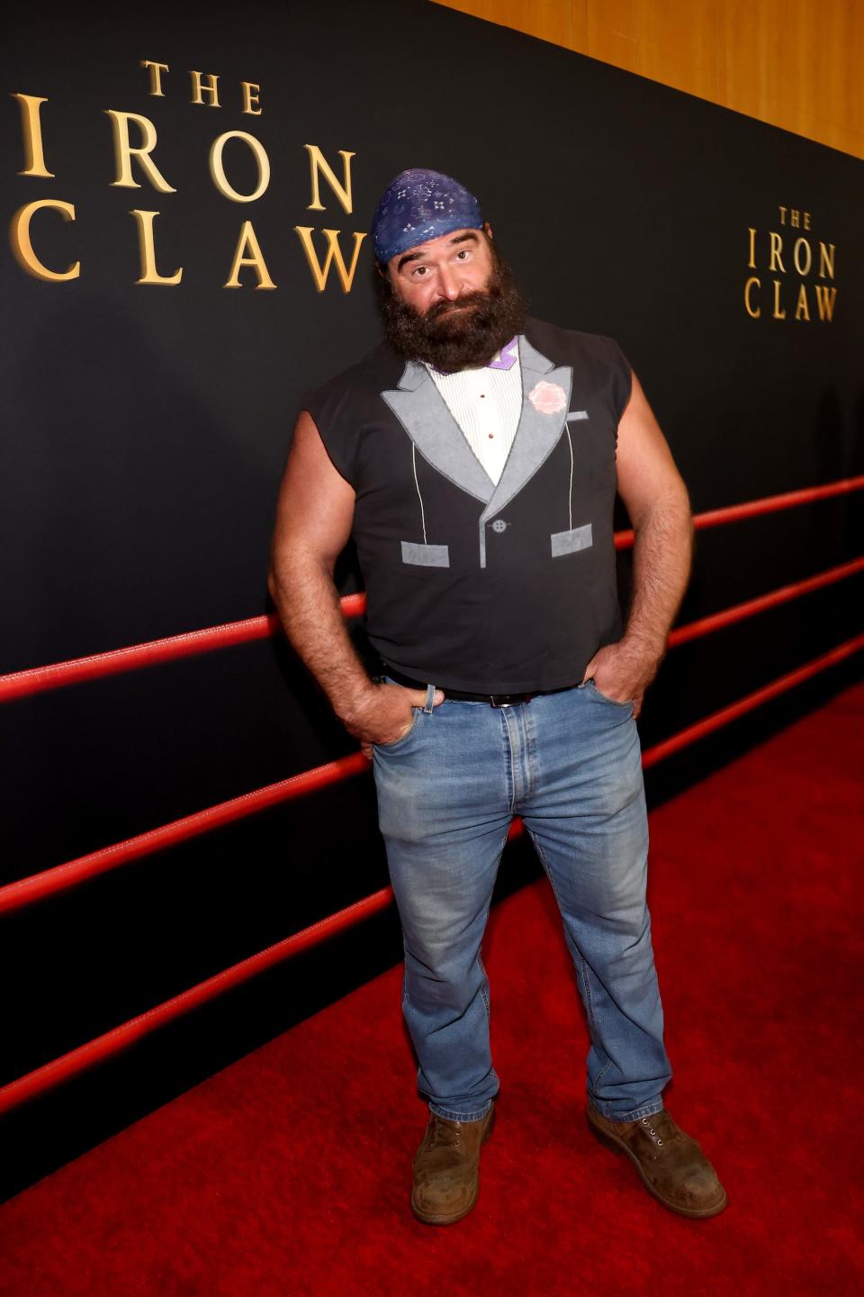 Cazzy Cereghino wearing a bandana, a faux tuxedo vest and jeans at "The Iron Claw" premiere