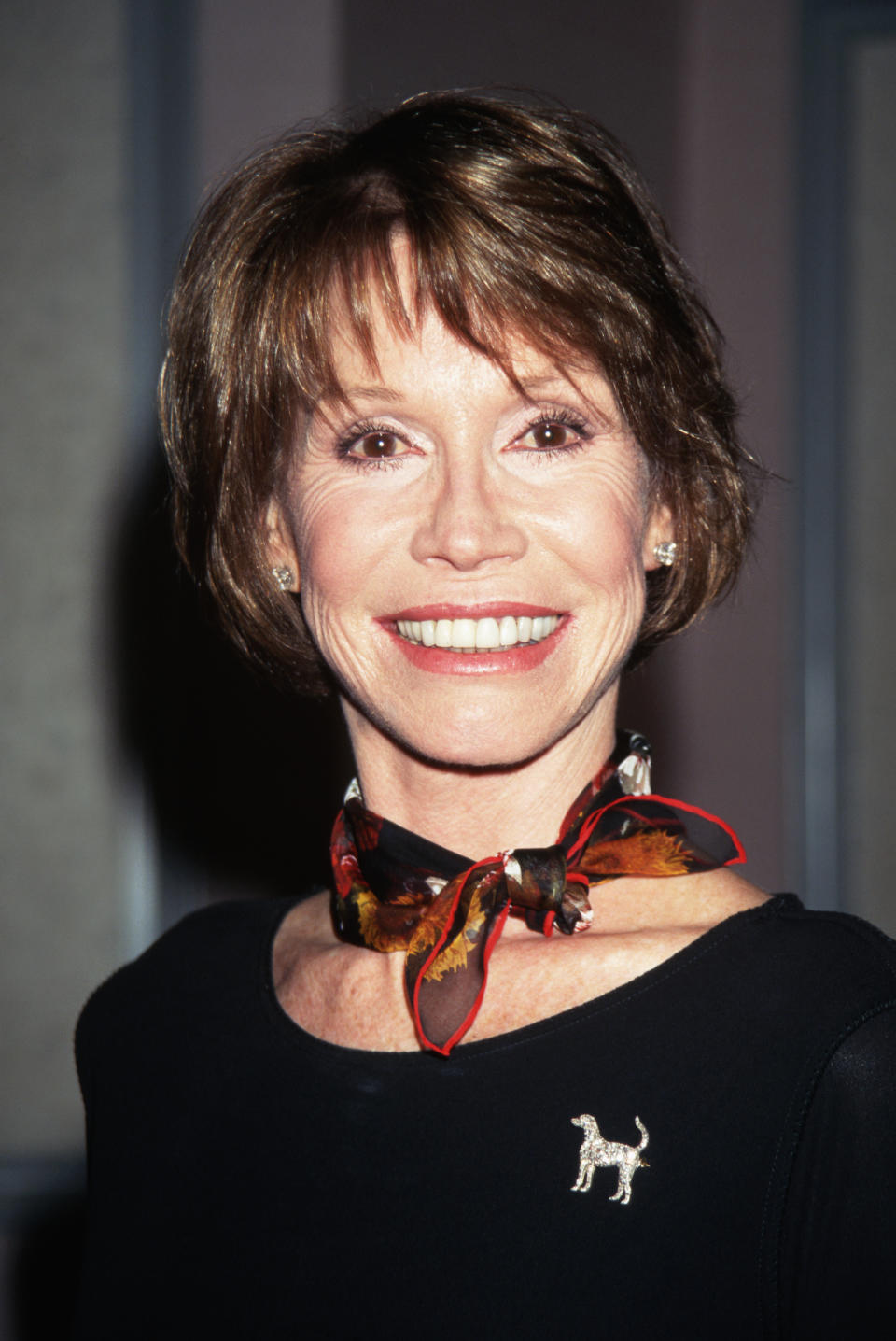 Close-up of Mary smiling and wearing a shirt and neck scarf