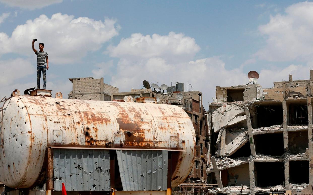 A Syrian youth takes a photo on top of a bullet-riddled water container on the destroyed Thalateen Street in the Yarmuk Palestinian refugee camp on the southern outskirts of the capital Damascus - AFP