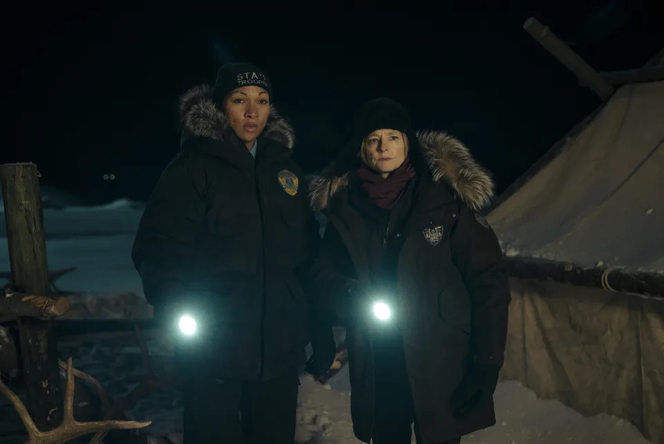 Two women in thick winter coats and hats holding flashlights while out in the snow at night; still from "True Detective: Night Country"