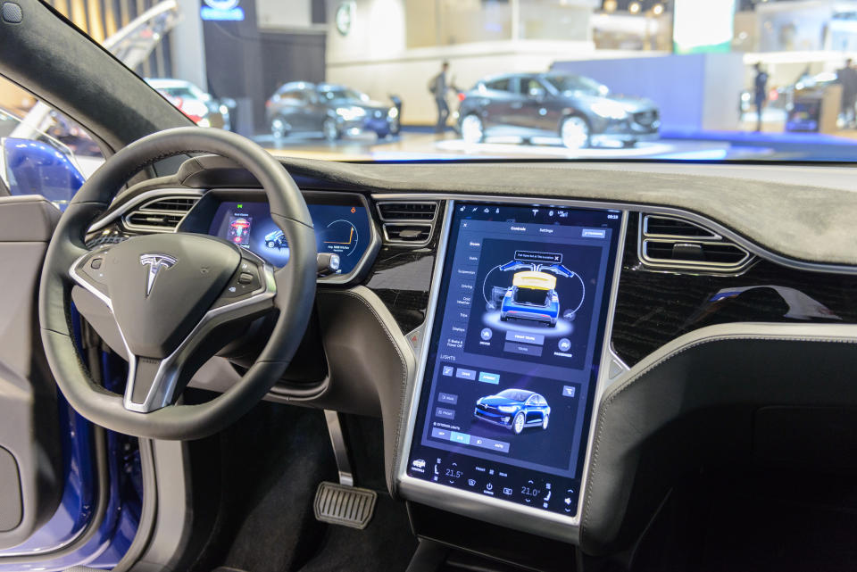 Brussels, Belgium - January 13, 2017: Luxurious interior on a Tesla Model X 90D full electric luxury crossover SUV car with a large touch screen and dashboard screen. The car is fitted with leather seats and aluminium details. The Model X uses falcon wing doors for access to the second and third row seats. The car is displayed on a motor show stand, with lights reflecting off of the body. There are people looking around and other cars on display in the background.