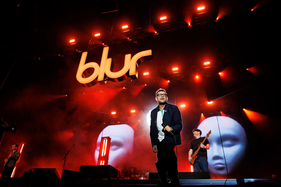 Damon Albarn von Blur steht auf einer Bühne mit roten Lichtern hinter sich