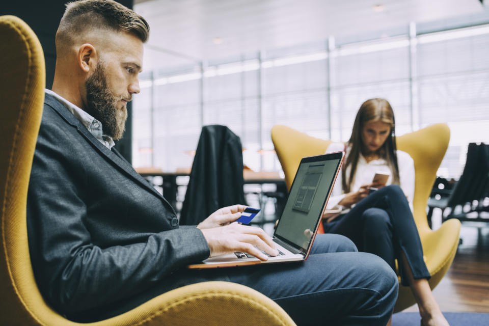 Side view of businessman holding credit card while using laptop at airport