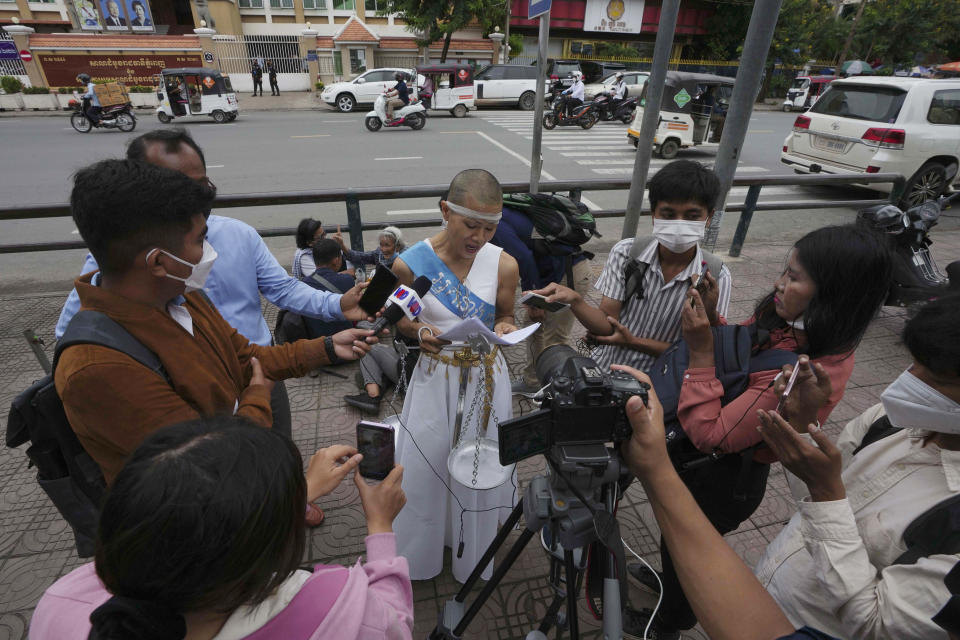 Cambodian-American lawyer Theary Seng, dressed in a pageant costume that reads "Lady Justice", reads a document to media outside Phnom Penh Municipal Court in Phnom Penh, Cambodia, Tuesday, May 3, 2022. Tuesday is the the final day of hearings for her trial on treason and a related charge for which she could receive a prison sentence of up to 12 years. (AP Photo/Heng Sinith)