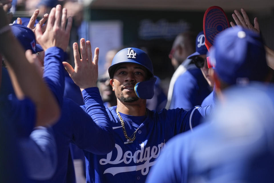 Los Angeles Dodgers' Mookie Betts celebrates in the dugout after scoring off of a triple by Shohei Ohtani during the second inning of a spring training baseball game against the Colorado Rockies in Phoenix, Sunday, March 3, 2024. (AP Photo/Ashley Landis)