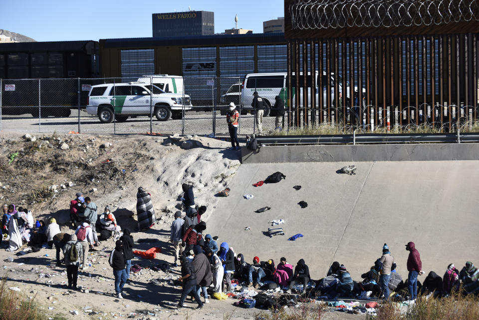 FILE - Migrants wait to cross the U.S.-Mexico border from Ciudad Juárez, Mexico, next to U.S. Border Patrol vehicles in El Paso, Texas, Wednesday, Dec. 14, 2022. A federal judge on Thursday temporarily blocked the Biden administration from ending a Trump-era policy requiring asylum-seekers to wait in Mexico for hearings in U.S. immigration court. (AP Photo/Christian Chavez, File)