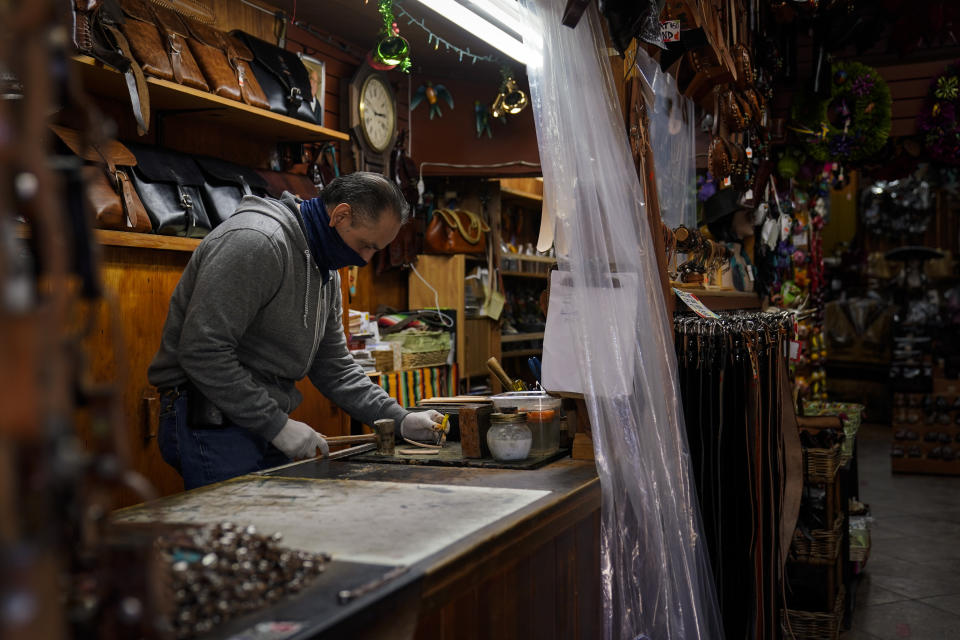 Leather artisan Armando Murillo works in his shop on Olvera Street in downtown Los Angeles, Wednesday, Dec. 16, 2020. Olvera Street, known as the birthplace of Los Angeles, has been particularly hard hit by the coronavirus pandemic, with shops and restaurants closed and others barely hanging on. Only a handful of businesses remain open on weekdays as tourism has cratered and downtown offices are closed and festive events held throughout the year have been canceled. (AP Photo/Jae C. Hong)