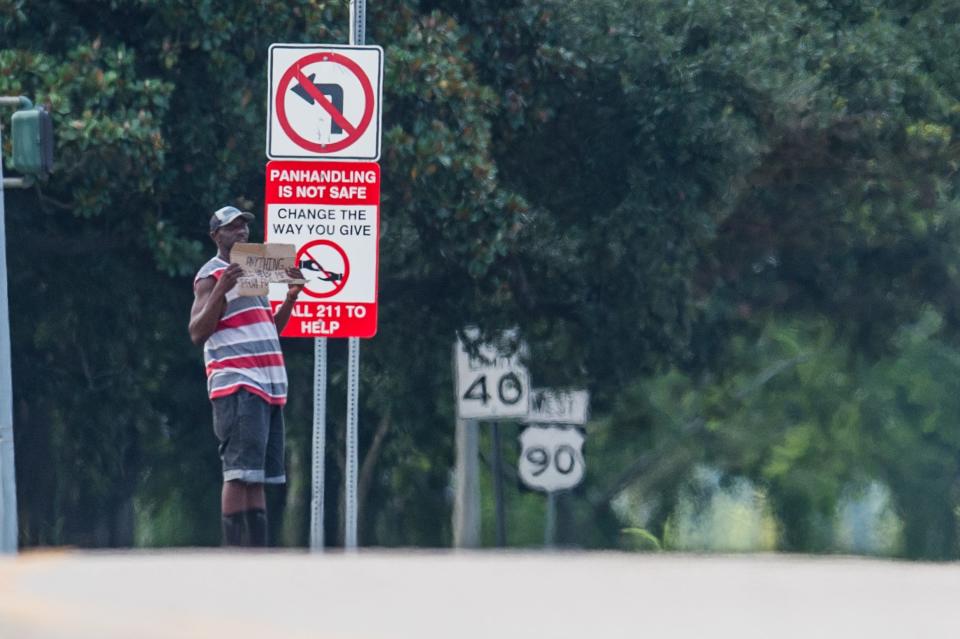 A man holds a sign asking for money beside a street sign installed last year that warns motorist that panhandling is not safe. Lafayette’s City Council may spend $1 million to help build a new shelter for people experiencing homelessness this month as the area’s unhoused population continues to grow.
