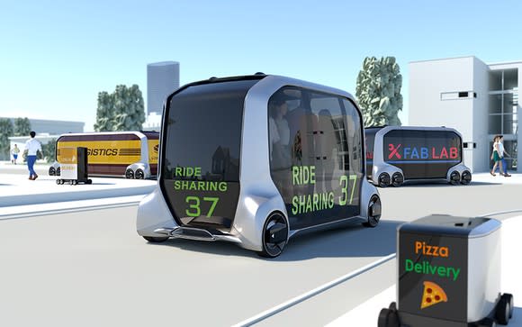 An artist's rendition of a mobile world. Different sizes of e-Palette, a box with wheels and mostly made of tinted glass windows, are on the road. Some of them are carrying mail, one pizza, another a ride-sharing service, and another a mobile retail store.