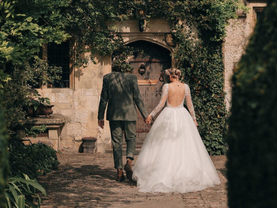 A couple walks towards a building in their wedding attire.