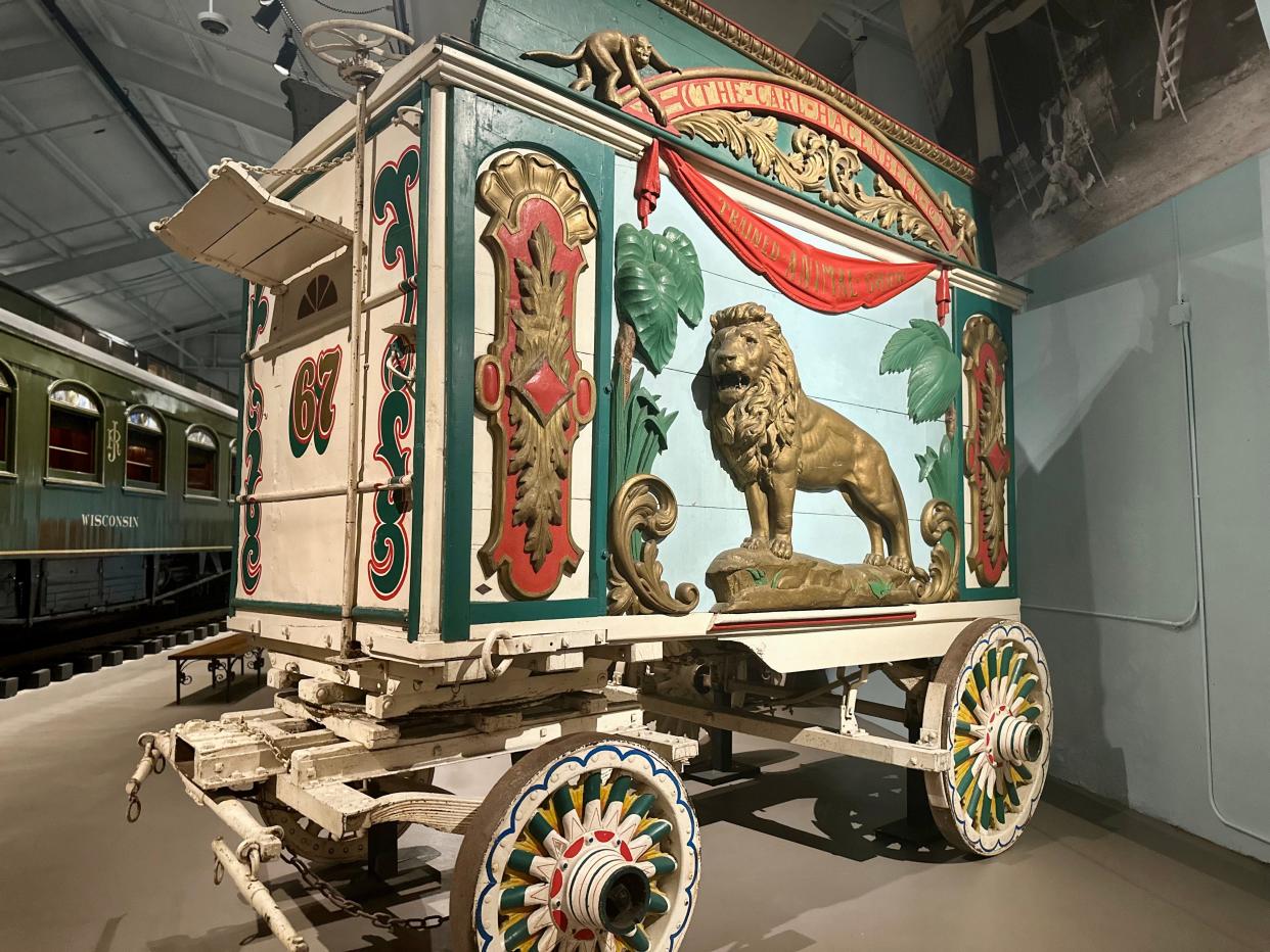 A circus wagon with an image of a lion, palm trees, and other gold, green, blue, and red details, in a museum