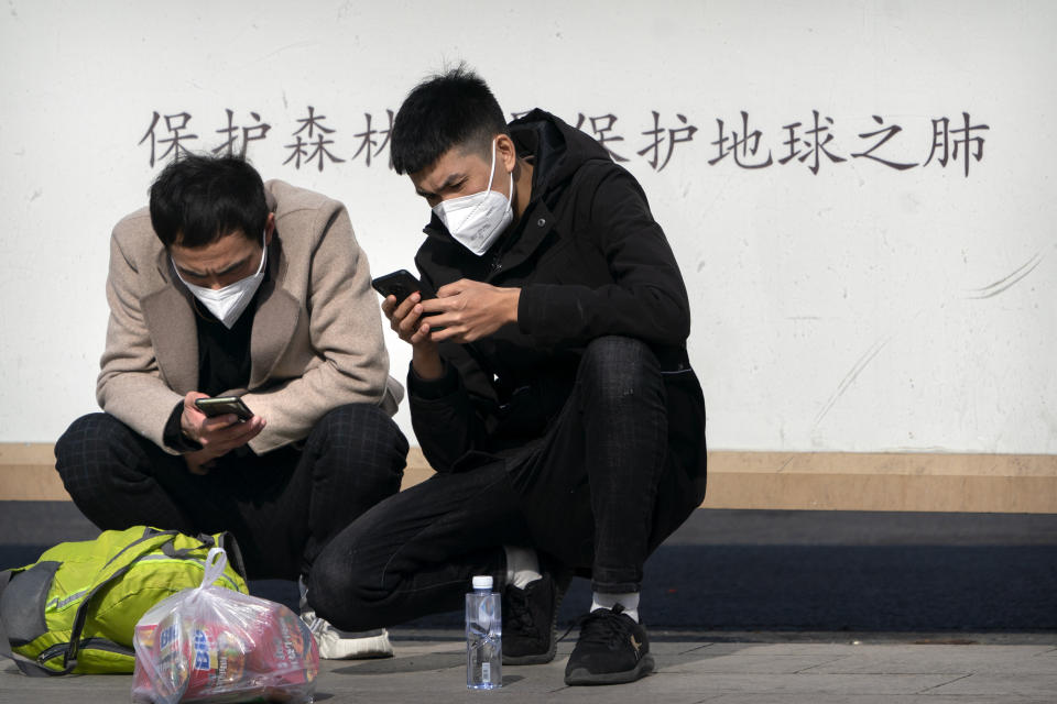 Travelers wearing face masks to protect against the spread of the coronavirus use their smartphones as they wait outside the Beijing Railway Station in Beijing, Wednesday, Feb. 10, 2021. China's internet watchdog is cracking down further on online speech, issuing a new requirement that bloggers and influencers have a government-approved credential before they can publish on certain topics. (AP Photo/Mark Schiefelbein)