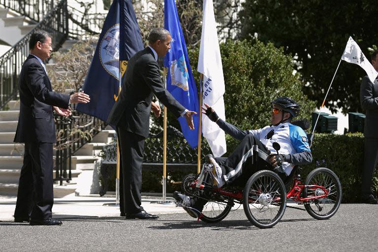 Veterans Affairs Secretary Eric Shinseki (L) and President Barack Obama give high-fives to one of the participants of the seventh annual Wounded Warrior Project's Soldier Ride on the driveway of the South Lawn of the White House, April 17, 2014
