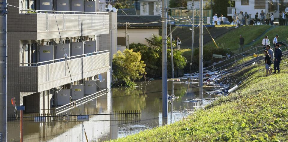 People look at a apartment building with its first floor under water in the residential area hit by Typhoon Hagibis, in Kawasaki, near Tokyo, Sunday, Oct. 13, 2019. Rescue efforts for people stranded in flooded areas are in full force after a powerful typhoon dashed heavy rainfall and winds through a widespread area of Japan, including Tokyo.(Kyodo News via AP)