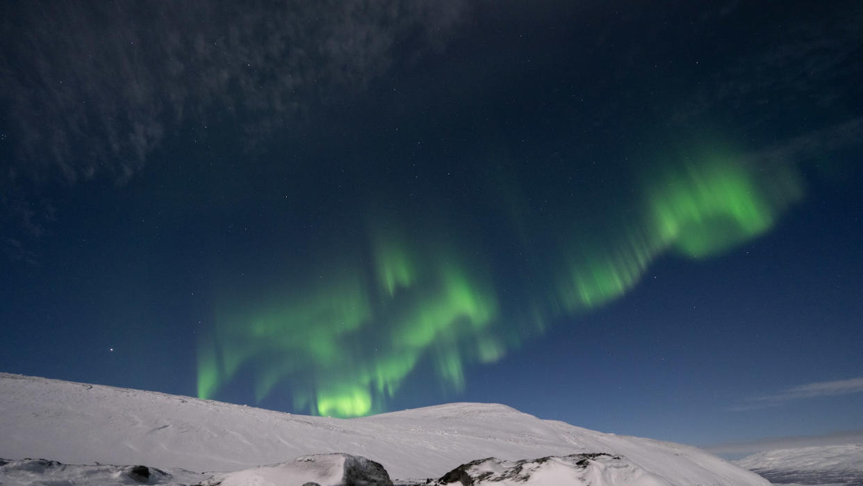  Northern lights appear as green ribbons of light across the sky with a snowy mountain below. . 