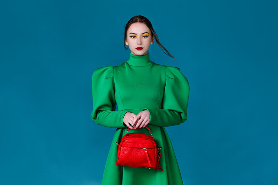 A portrait of an attractive young woman wearing green beautiful dress, holding a red purse