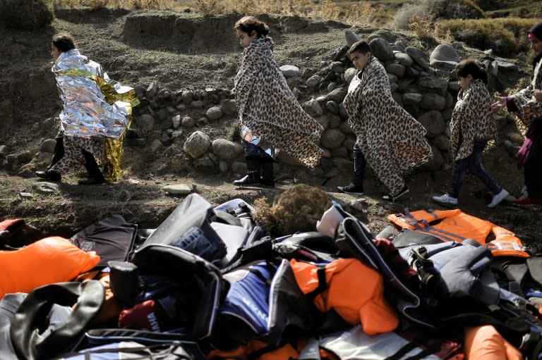 Refugees and migrants walk past discarded lifejackets as they arrive on the Greek island of Lesbos after crossing the Aegean sea from Turkey