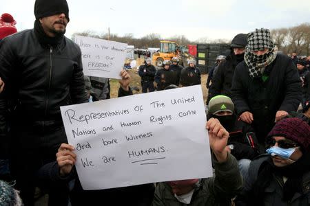 French CRS rioit police stand near Iranian migrants with a message, "Representatives of the United Nations and Human Rights come and bare witness. We are Humans" during a protest against the partial dismantlement of the shanty town called the "Jungle" in Calais, France, March 2, 2016. REUTERS/Pascal Rossignol