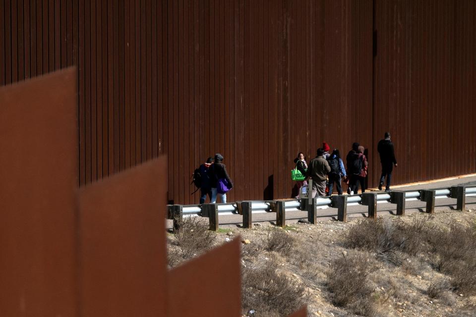 A group of migrants, mostly from African countries, walk to an open gate on the border wall to be processed by the border patrol after crossing the US-Mexico border seen from Tijuana, Baja California state, Mexico, on November 11, 2022. / Credit: GUILLERMO ARIAS/AFP via Getty Images