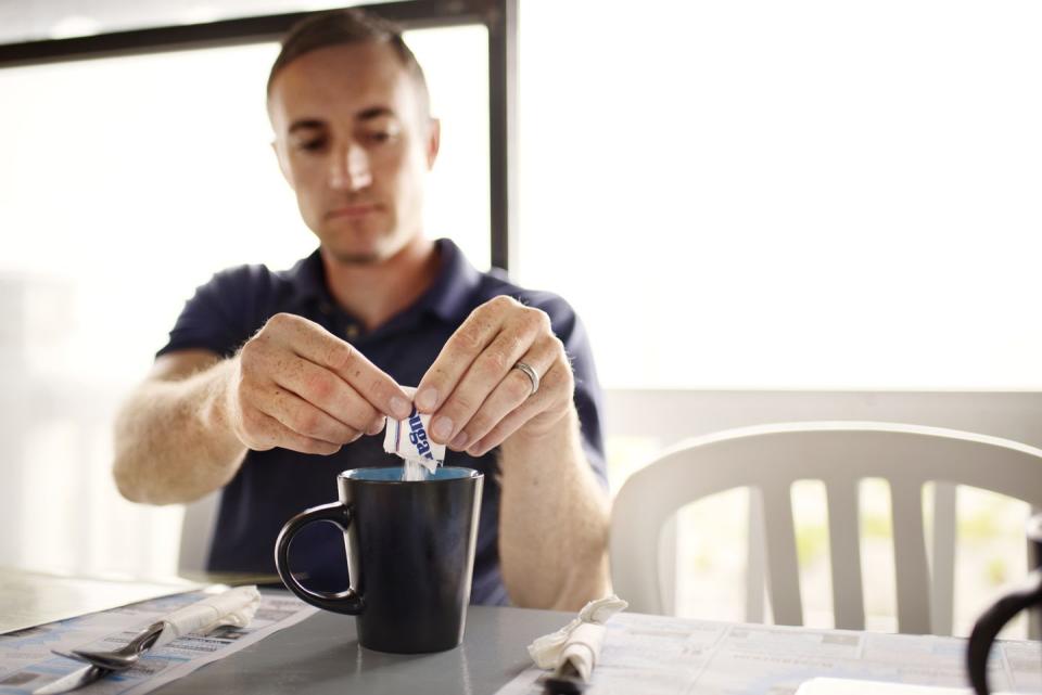 man adding sugar to coffee mug at restaurant table